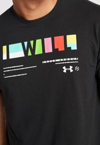 Svart bomulls t-shirt med ett flerfärgat geometriskt tryck och text. Under Armour-logotypen visas i nedre högra hörnet.