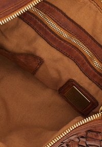 Interno in pelle marrone di una borsa con un comparto principale, due tasche con zip e un design tessuto, intrecciato, con dettagli in hardware dorato.