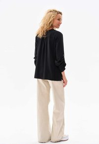 Schwarzes Langarmshirt mit gerafftem Rückendetail, kombiniert mit beigen weiten Hosen und weißen Sneakern. Glattes Material und entspannte Passform.