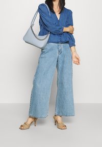 Džínová košile s nabíranými rukávy, světle modré široké kalhoty, béžové sandály na podpatku a světle modrá kabelka s řetízkem.