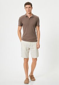 Brun mattopolo, ljusbeige linnebyxor och ljusbruna slip-on skor. Modellen står mot en enkel vit bakgrund.