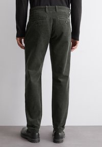 Tmavě zelené kordové kalhoty se rovnými nohavicemi, dvěma zadními kapsami na knoflíky a poutky na opasek, doplněné černými botami.