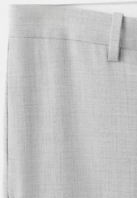 Tissu gris clair avec un motif quadrillé subtil, comprenant une ceinture et des passants de ceinture sur un vêtement ajusté.