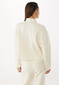 Maglione a maniche lunghe, di colore crema, con collo alto e spalle cadenti. Realizzato in un morbido tessuto a maglia testurizzata, offre una vestibilità rilassata.