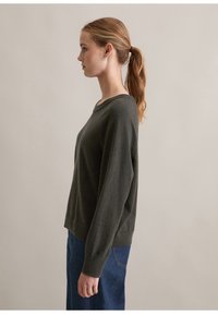 Mörkgrön stucktröja med rund hals, långa ärmar och en avslappnad passform, kombinerad med en blå jeanskjol. Slät textur, minimalistisk design.