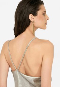 Camisola metallica argento con spalline sottili, design con schiena scoperta, che mostra una texture liscia e uno stile minimalista. L'accessorio include un orecchino pendente.