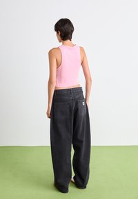 Un débardeur rose court et un jean noir ample, avec une étiquette à la taille, deux poches arrière et une texture lisse.