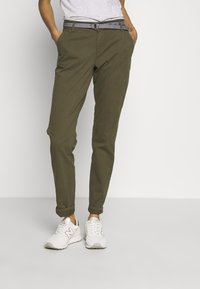 Olive green chinos with a relaxed fit, cuffed ankles, and a striped black-and-white belt, paired with white athletic shoes.