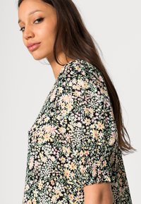 Blusa com estampado floral, com mangas curtas e bufantes, fundo preto, flores coloridas em rosa, amarelo e verde, com punhos franzidos.