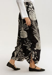 Černá široká sukně s bílým botanickým potiskem, s detaily stopkového šněrování na stranách a texturovanou látkou; kombinovaná s černými plochými botami.