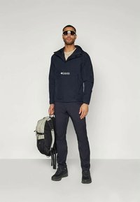 Mørkeblå lett jakke med en frontlomme, sammen med svarte bukser og robuste svarte sko. En grå og svart ryggsekk bæres.