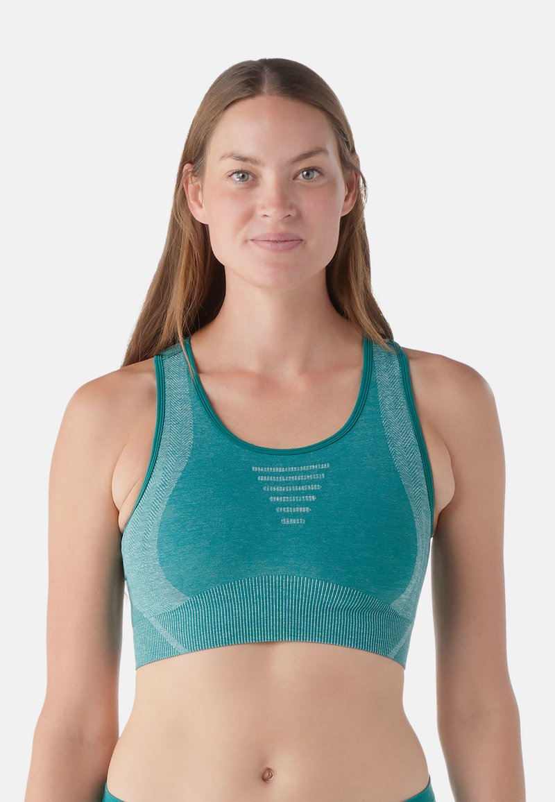 Teal sportbehå med en åtsittande design, ribbad textur, breda axelremmar och meshdetalj i mitten. Sömfritt utförande för komfort.