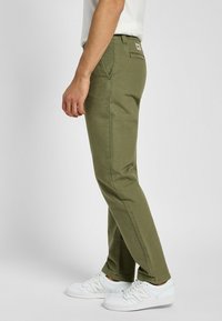 Oliwkowe spodnie z bawełnianej mieszanki, z prostymi nogawkami, usztywnionym paskiem w talii oraz kieszeniami bocznymi. Noszone z białymi trampkami.