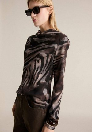 Long-sleeve top featuring a black and brown zebra print, made of lightweight fabric. Paired with dark pants and layered bangle accessories.