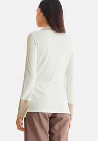 Langsleeve top in off-white geribbeld materiaal, met beige accenten op de manchetten. Gladde textuur en fitted ontwerp met een eenvoudige kraag.