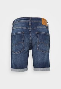 Tummansinisiä farkkushortsit, joissa on käännetyt lahkeet, kaksi takataskua ja ruskea nahkainen brändilappu vyötäröllä.