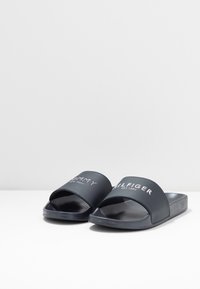 Marina slidesandaler har en bred rem med vit text, slät syntetisk material, öppen tå-design och platt, texturerad sula.