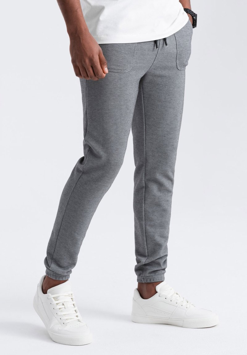 Pantalones de chándal grises hechos de un tejido texturizado, con bolsillos y cintura con cordón. Combinados con zapatillas blancas para un look casual.