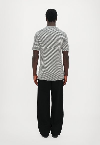 Chemise pour homme à manches courtes dans un motif texturé gris et blanc, associée à un pantalon ample noir. Le tissu semble léger et respirant.