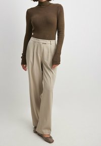 Ruskea, ribbineulottu pooloneule, beigeä leveälahkeiset housut ja harmaat litteät kengät, joissa on rusetit. Ylhäällä sileät materiaalit ja istuva siluetti.