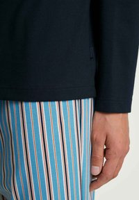 Marineblauwe blouse met lange mouwen van een gladde stof, gecombineerd met blauwgestreepte broek met oranje en witte accenten. Zichtbaar logo-label op de blouse.
