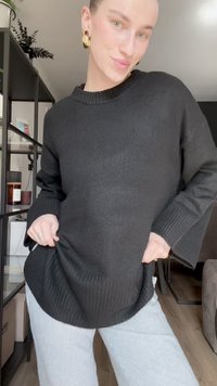 Black ribbed knit sweater with a rounded neckline, paired with white vertical striped wide-leg pants. The texture appears soft and cozy.