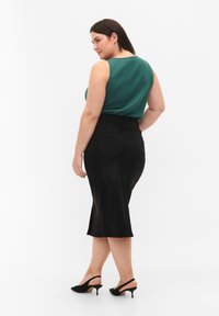 Top sin mangas verde, falda negra hasta las rodillas con bolsillos traseros y tacones de sling-back negros. Textura suave, silueta ajustada.