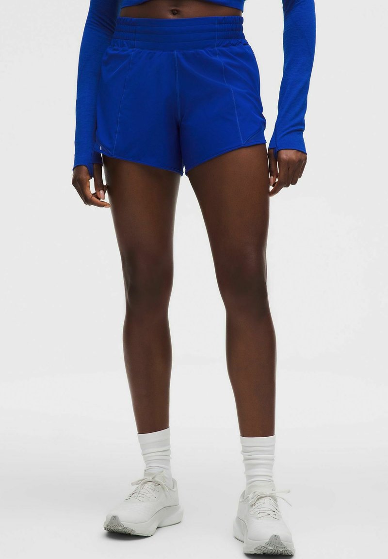 Zili sporta šorti ar augstu elastīgu jostu, ar sānu kabatām un gludu, vieglu audumu. Nēsāti kopā ar baltām sporta apaviem.