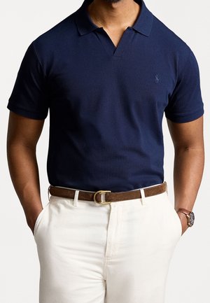 Granatowa koszulka polo z klasycznym kołnierzem, krótkimi rękawami i subtelnym logo. Połączona z kremowymi spodniami i brązowym paskiem.