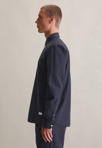 Marineblauwe langermige shirt van gestructureerde stof, met een knopsluiting kraag en een borstzak, voorzien van knoopaccenten op de manchetten.