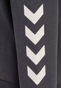 Grå sweatshirt med et tekstureret stof, der har hvide chevronmønstre på ærmet, hvilket understreger et moderne design.