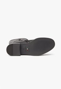 Stivale in pelle nera con suola in gomma piatta, caratterizzato da una texture a righe, dettagli di branding e una marcatura della taglia sulla suola.