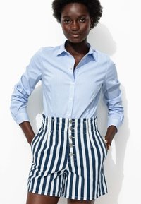 Chemise à rayures bleues et blanches avec des boutons, associée à un short taille haute à rayures marines et blanches, comportant cinq boutons et des poches latérales.