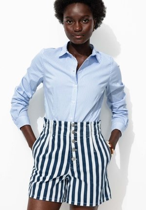 Chemise à rayures bleues et blanches avec des boutons, associée à un short taille haute à rayures marines et blanches, comportant cinq boutons et des poches latérales.