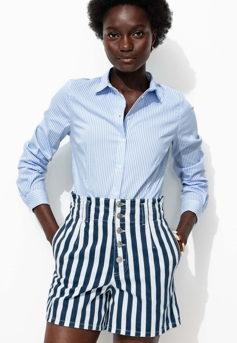 Chemise à rayures bleues et blanches avec des boutons, associée à un short taille haute à rayures marines et blanches, comportant cinq boutons et des poches latérales.