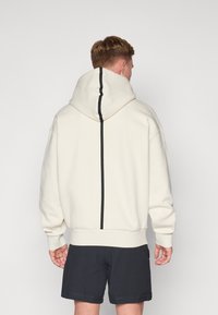 Hoodie in gebroken wit met een zwarte verticale streepdetail op de achterkant, geribde zoom en manchetten, en een relaxte pasvorm.