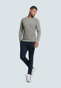 Grijze geribbelde trui met ronde hals, gecombineerd met donkere slim-fit broeken en witte sport sneakers. Gebreid textuurdetail doorheen.