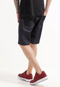 Tmavé džínové šortky s volným střihem, viditelným šitím a dvěma zadními kapsami. Kombinovány s červenými sportovními botami s bílými podrážkami.