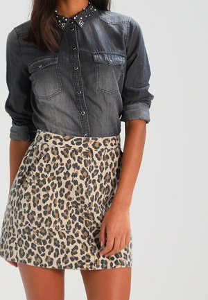 Chemise en denim avec col clouté, deux poches avant, associée à une jupe beige à motifs léopard avec poches, mettant en valeur des textures contrastées.