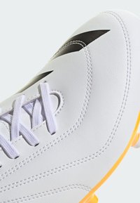 Hvide fodboldstøvler med sorte accenter, struktureret syntetisk overdel og gul sål. Har lige snørebånd og syet detaljering.