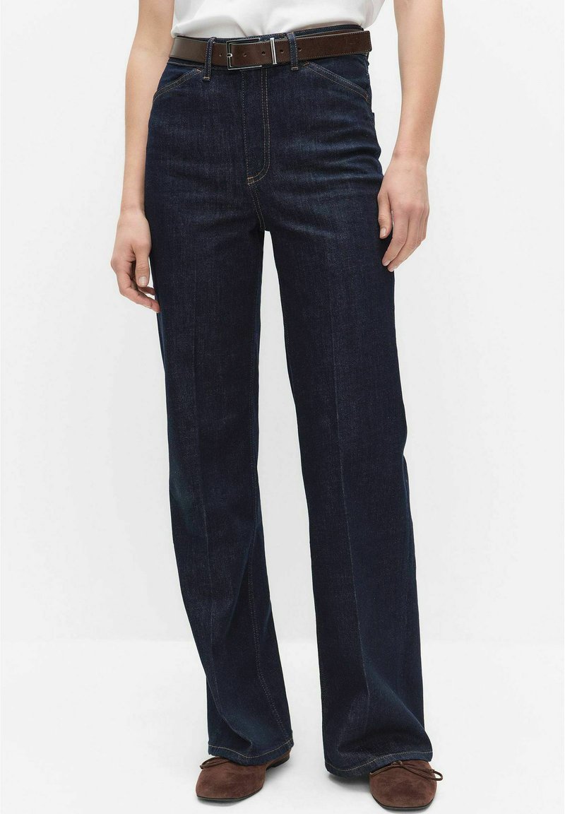 Donkerblauwe spijkerbroek met rechte pijpen, hoge taille en een bruine leren riem. Zichtbare stiksels en klassieke vijfzakkenontwerp.