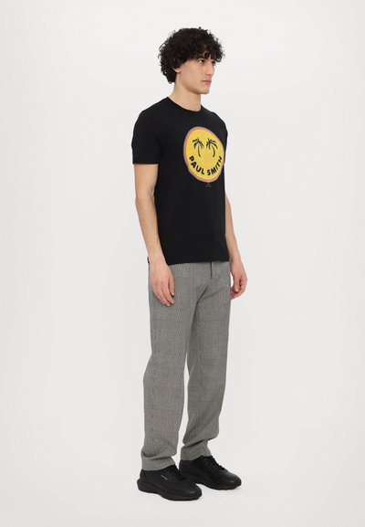 T-shirt noire avec un graphique rond jaune représentant des palmiers et le texte "PAUL SMITH". Associé à un pantalon en plaid gris et des baskets noires.