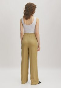 Wijdvallende pantalons in een lichte olijfgroene tint, gemaakt van een textuurstof. Voorzien van een elastische tailleband en gecombineerd met een witte tanktop.