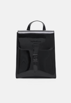 Sac à dos en cuir noir brillant avec poignée supérieure, rabat avant et fermeture à boucle, affichant le logo Dr. Martens embossé à l'avant.