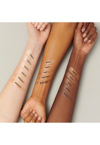 Trois bras avec des teintes de peau variées présentent des échantillons étiquetés CLAIR, MOYEN, FONCÉ et RICHE, mettant en avant différentes teintes de fond de teint.