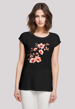 Schwarzes T-Shirt mit floralem Design in pinken und pfirsichfarbenen Blumen, kurzen Ärmeln und rundem Ausschnitt, kombiniert mit weißen Hosen.