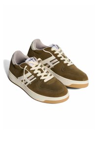 Sneaker in suede marrone con accenti bianchi, punta rotonda e suola in gomma piatta; presenta lacci crema e branding sulla linguetta e sul lato.