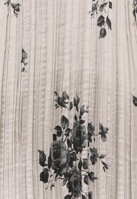 Tessuto plissettato con una base beige chiaro e motivi floreali neri. La trama appare liscia, con linee verticali che valorizzano il design.