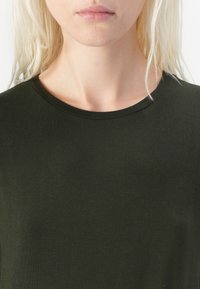Tmavě zelené, přiléhavé tričko s kulatým výstřihem. Hladká textura, krátké rukávy a jednoduchý design bez vzorů nebo akcentů.