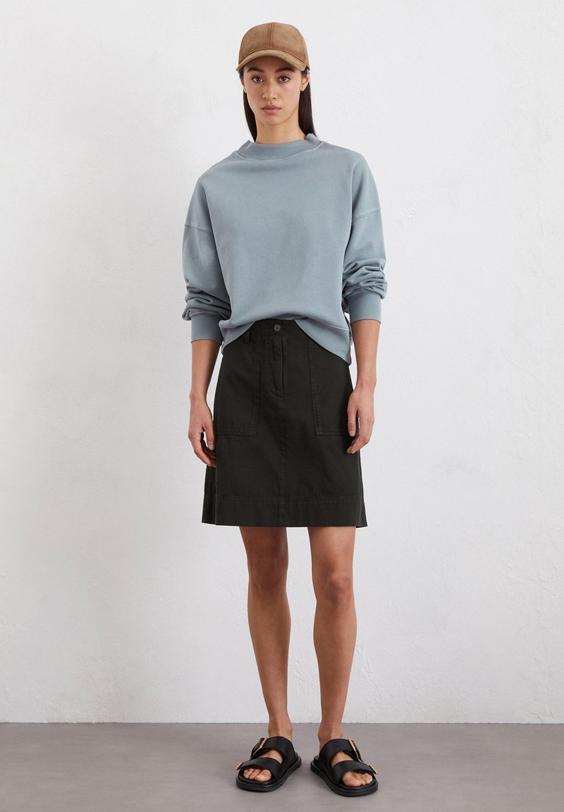 Lichtblauwe oversized sweatshirt, zwarte rok tot de knie met voorkwabben, bruine pet, en zwarte sandalen met een gespdetail.